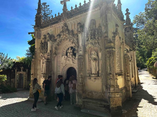 Photo of a small chapel with ornate stucco exterior - visitors are entering through its arched doorway