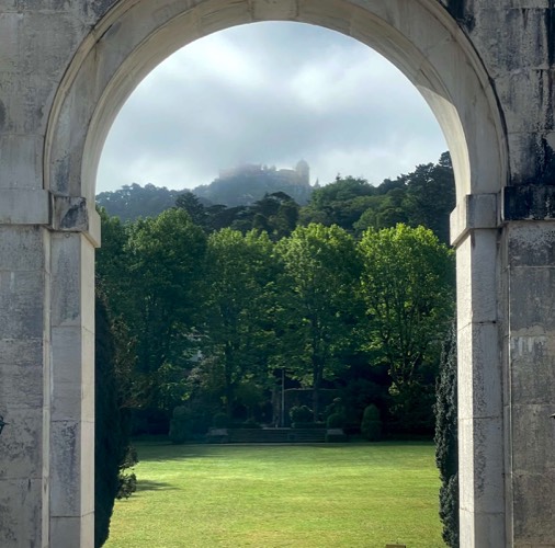 A misty view of a palace on top of a hill seen through an an archway in the foreground
