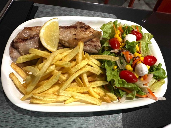 A white oblong plate laden with Portuguese salted pork with salad and fries